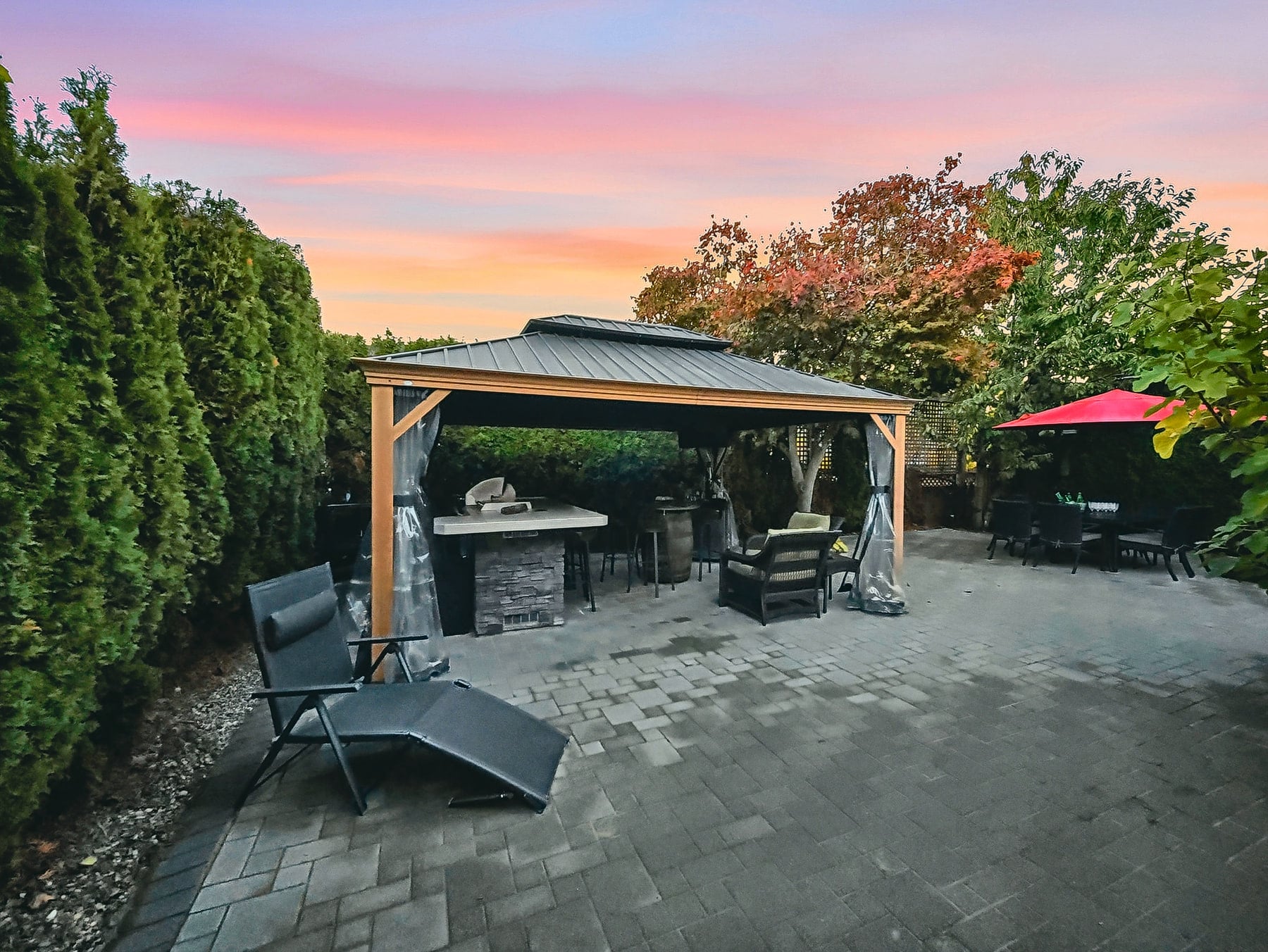 Landscaped backyard with paved patio, mature hedges and an outdoor dining area