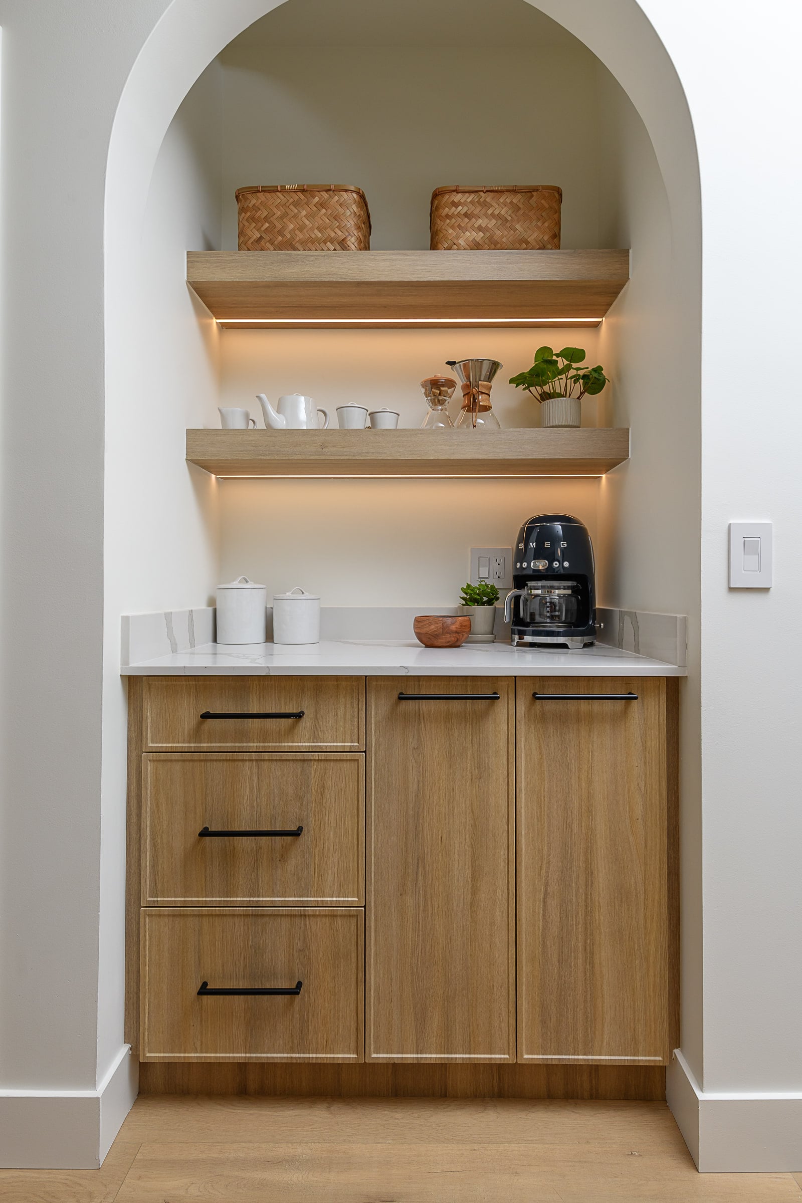 The arch-enclosed beverage bar with lit shelves, behind a quartz island