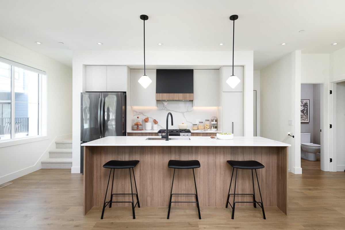 Showhome kitchen with a central island, three black stools and a black range hood